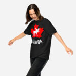 Front of Canada Moose black unisex garment-dyed heavyweight t-shirt on girl showing maple leaf & moose print. Canada written below.