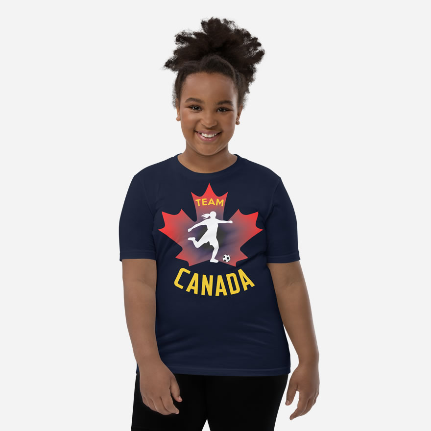 Front of Girl's Soccer navy youth staple t-shirt on girl. Player kicking ball silhouette on red maple leaf. Says Team Canada.