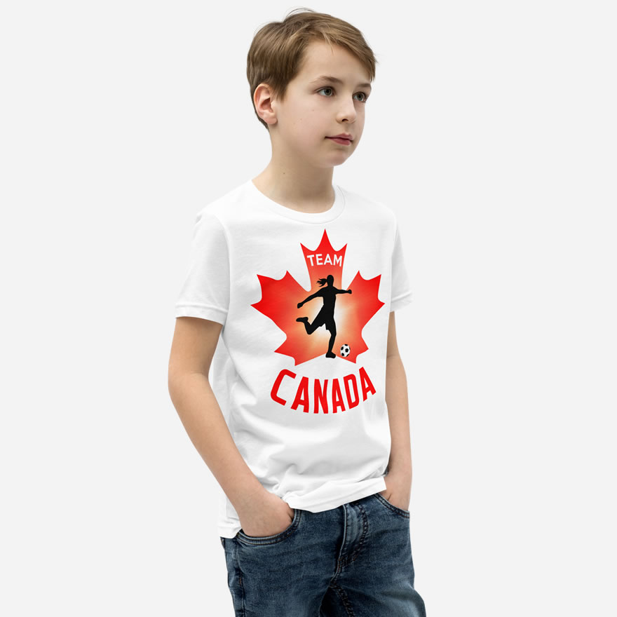 Front of Girl's Soccer white youth staple t-shirt on boy. Player kicking ball silhouette on red maple leaf. Says Team Canada.