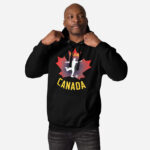 Front of Men's Soccer hoodie black unisex premium pullover on man. Player kicking ball silhouette on maple leaf. Says Team Canada.