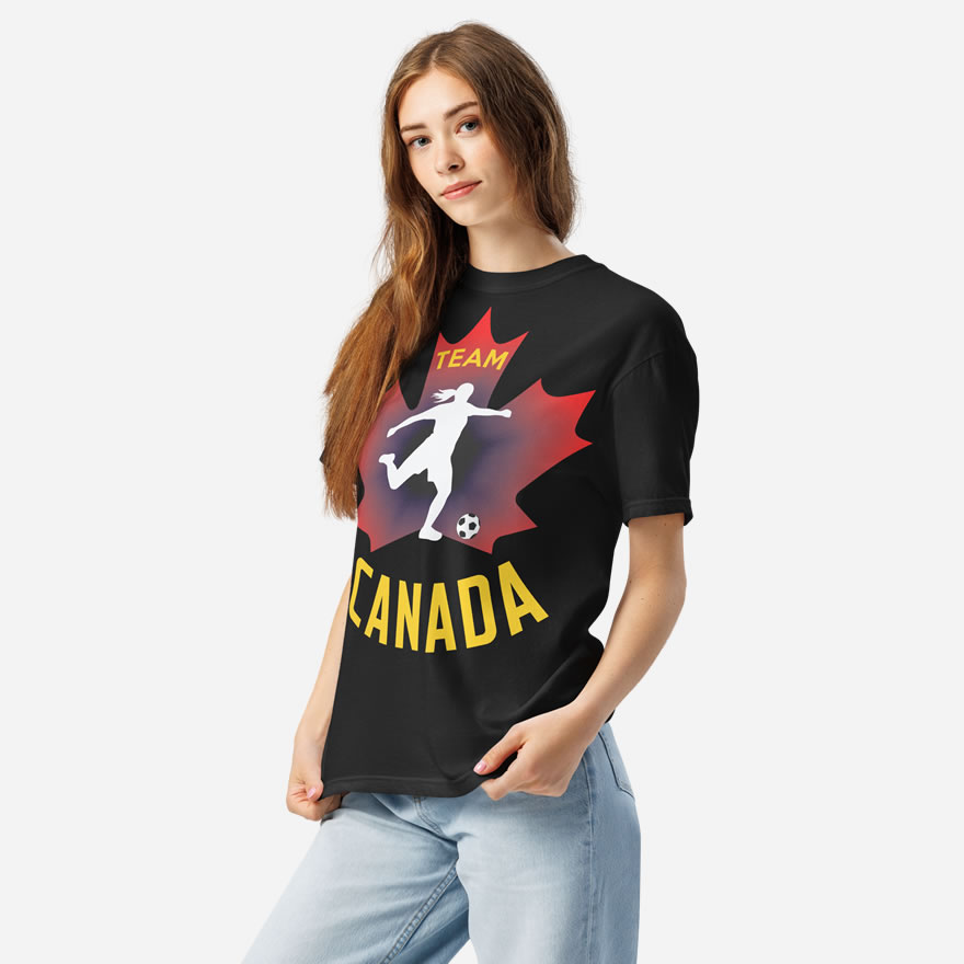 Front of Women's Soccer black heavyweight tee on woman. Player kicking ball silhouette on red maple leaf. Says Team Canada.
