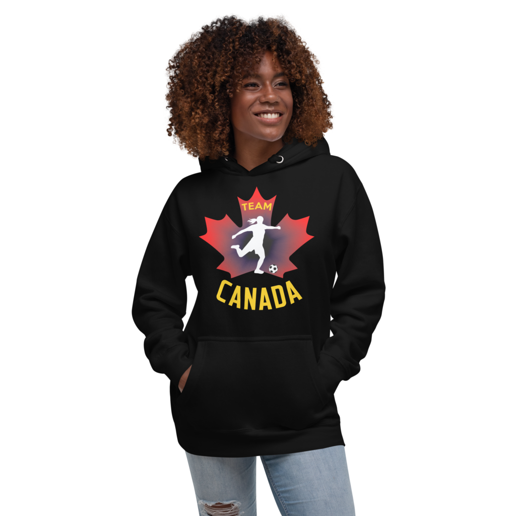 Front of Women's Soccer hoodie black unisex premium pullover on woman. Player kicking ball silhouette on maple leaf. Says Team Canada.