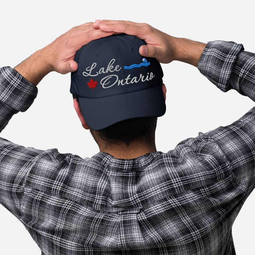 Front of Lake Ontario navy classic dad hat on model showing 'Lake Ontario' embroidered white along with red maple leaf & blue wave.