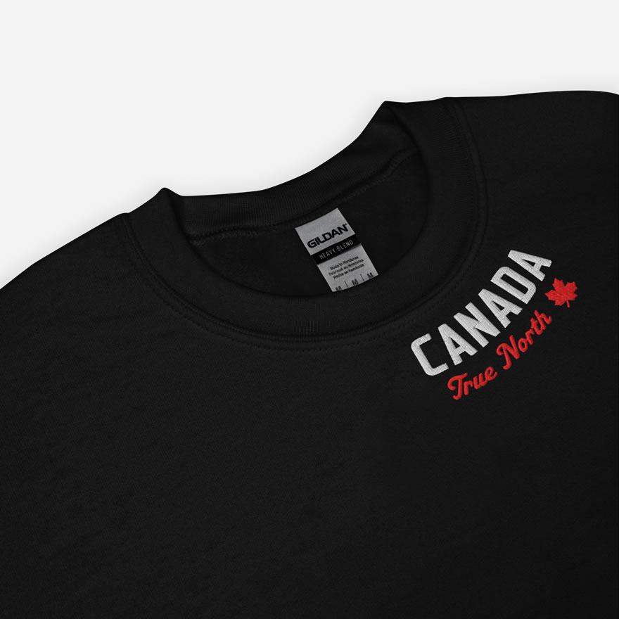 Close up of black Canada True North sweatshirt with words Canada in white, True North red and a red maple leaf curved along neckline.