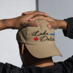 Front of Lake Ontario khaki classic dad hat on model showing 'Lake Ontario' embroidered black along with red maple leaf & blue wave.