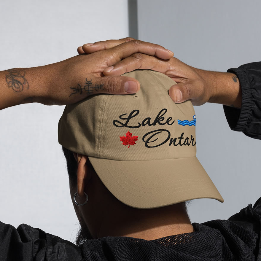 Front of Lake Ontario khaki classic dad hat on model showing 'Lake Ontario' embroidered black along with red maple leaf & blue wave.
