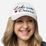 Front of Lake Ontario white classic dad hat on model showing 'Lake Ontario' embroidered black along with red maple leaf & blue wave.