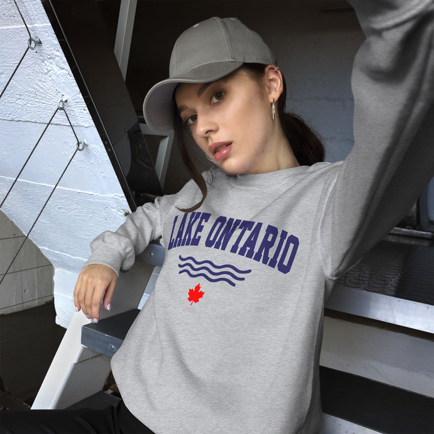 Front of Lake Ontario sport grey unisex crew neck sweatshirt on model with words Lake Ontario atop wavy lines (in navy) above a red maple leaf.